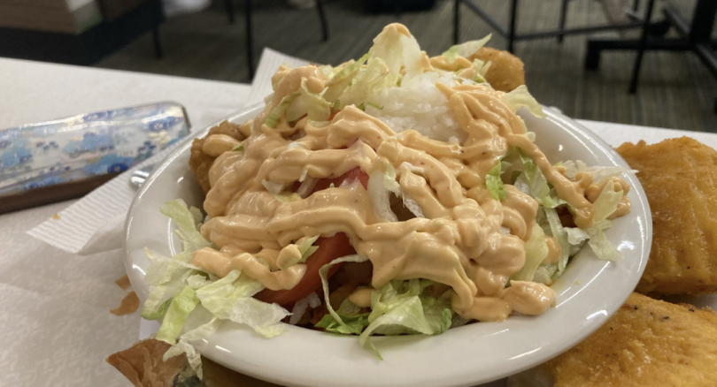 A white bowl holding a pile of vegetables and rice, with pale orange vegan chipotle mayo drizzled over the top