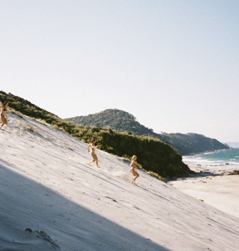 3 students running down a dune at a beach