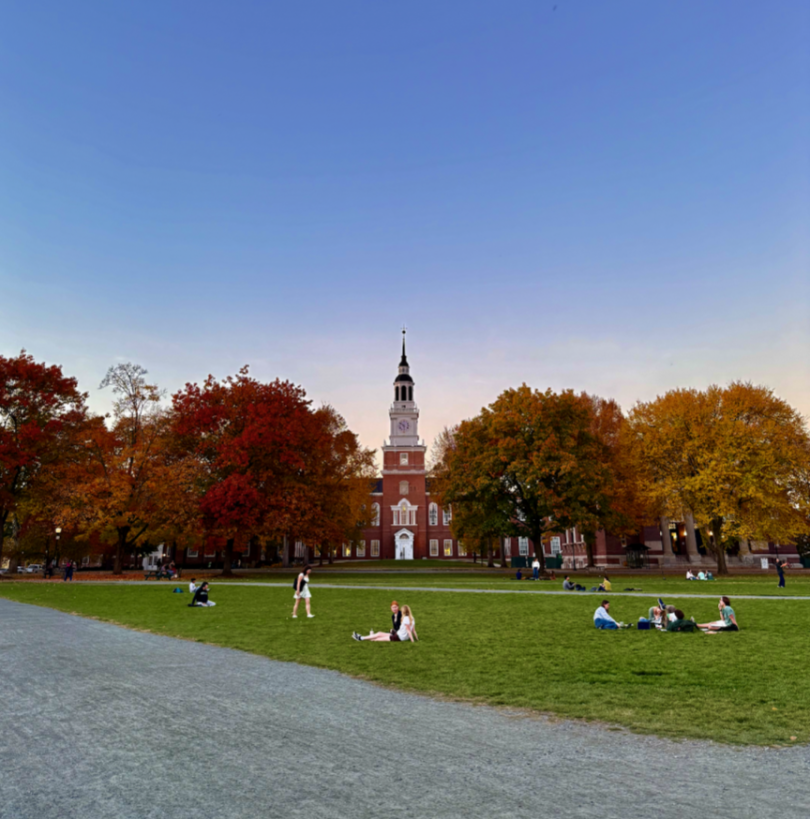 Baker-Berry Building in between trees with Fall foliage and people sitting on patches of grass enjoying a sunny day.