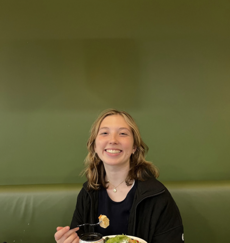 A girl is smiling at the camera with a green wall behind her.