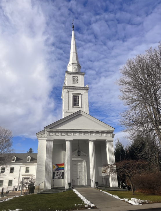 White church with a tower with the Progressive Pride Flag and the Black Lives Matter Flag hanging from the columns.