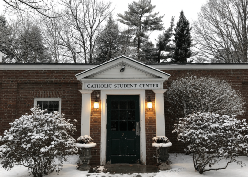 a door of a building named "Catholic Student Center" around trees with snow.