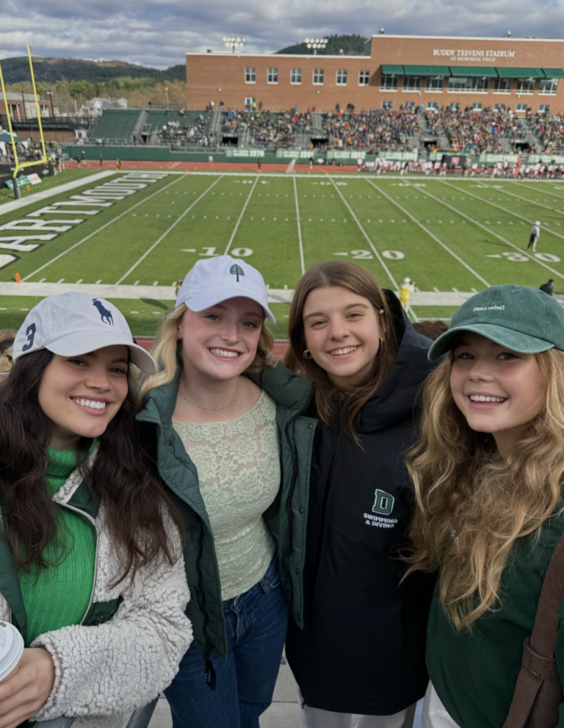 4 girls smiling and wearing green with a football field behind them.