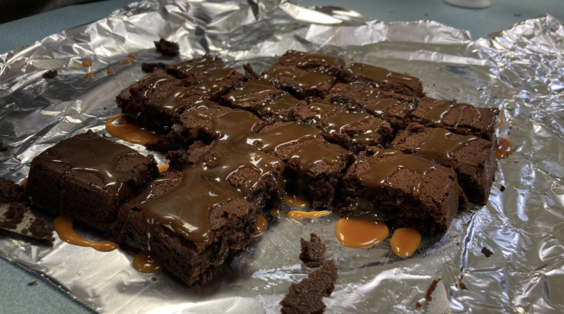 Rectangles of chocolate brownies with a caramel drizzle on a sheet of aluminum foil. 