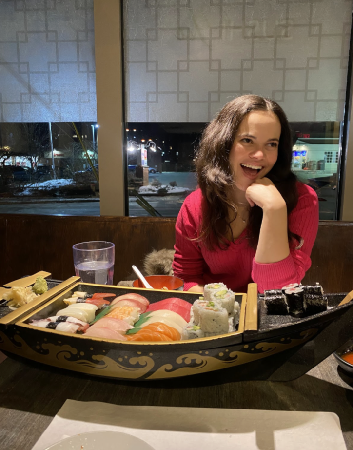 smiling girl with a boat of sushi in front.