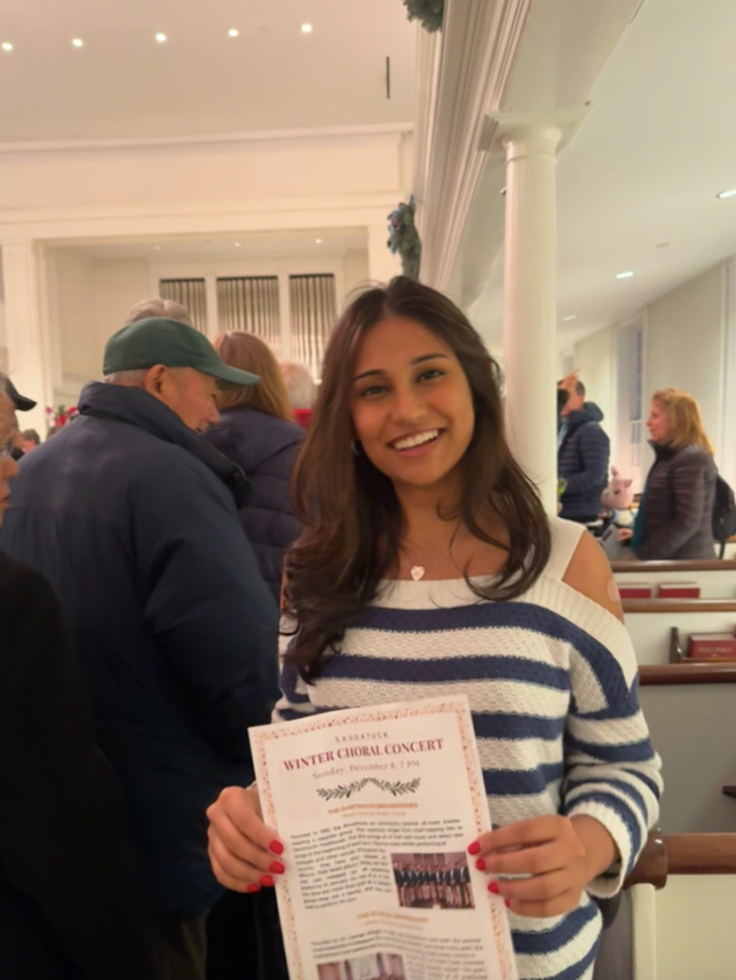 A woman stands in front of the camera, smiling and holding up a piece of paper. There are people getting ready to exit the church behind her.