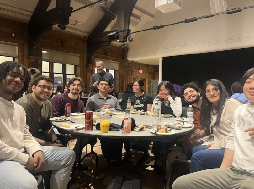 8 people sit gathered around a table in a dimly lit room