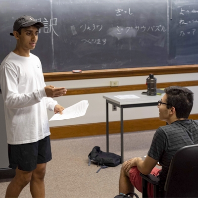 An image of a student standing in front of a blackboard with Asian characters on it running drill while a student sits in a chair opposite them