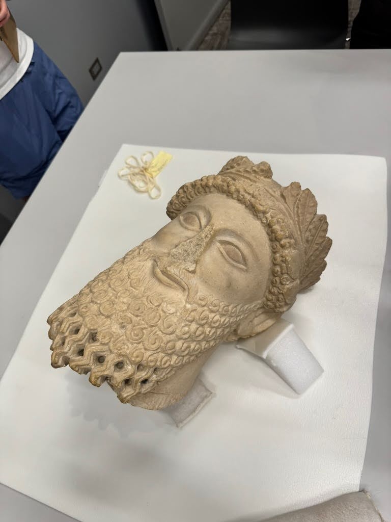 A Cypriot sculpture head laying on a white protective surface. The photo is taken from an angle above the sculpture, looking down on it.