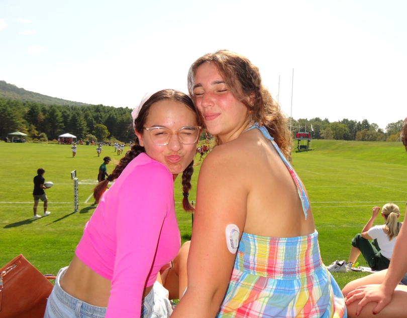 2 girls smiling at the camera while cheering on a rugby game in broad daylight