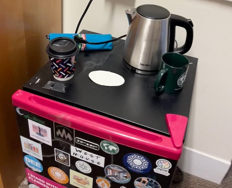 An image of a kettle and cups on top of a mini fridge inside a room