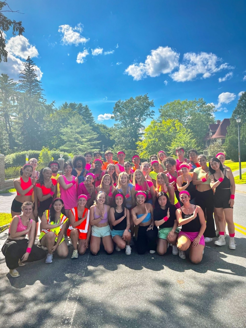  A group of people outside wearing neon clothes posing with one arm over the chest 