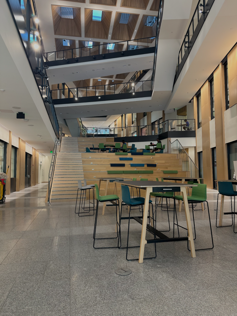 An atrium with tables and chairs, as well as windows in the ceiling and stairs.