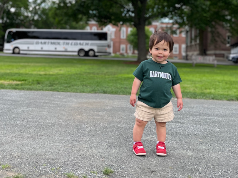 a baby stands on the Dartmouth Green with a Coach bus behind him