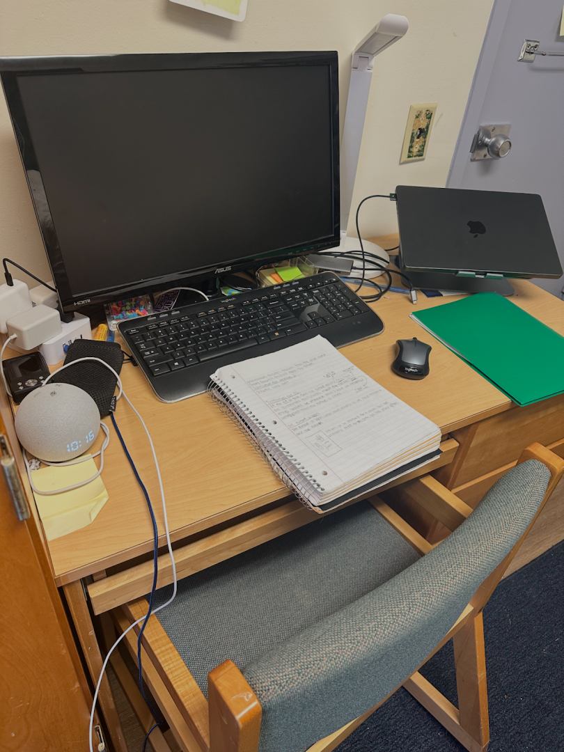 Picture of desk with a laptop, monitor, folder, and an open notebook.
