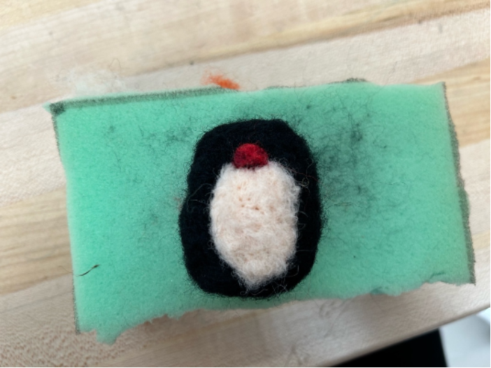 The beginning of a needle-felted penguin design on green foam