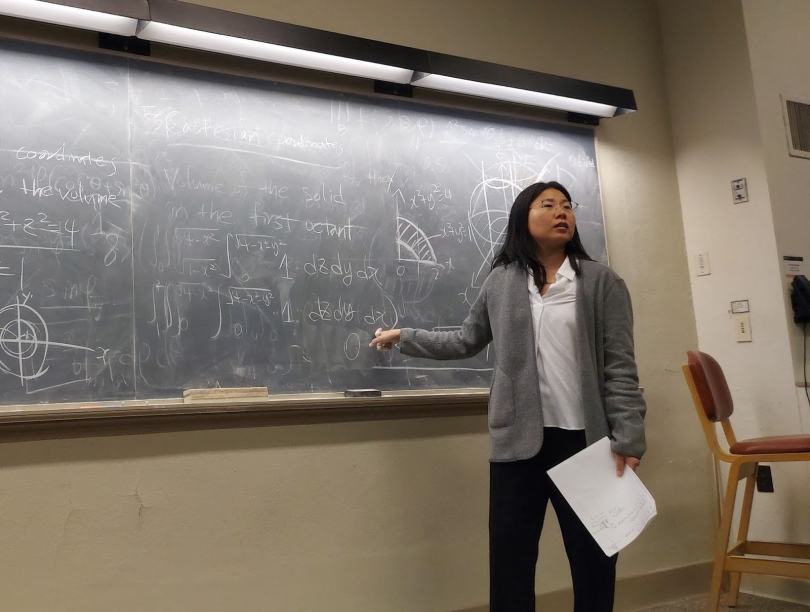 A professor teaching math, standing in front of a board dirty from all the chalk. 