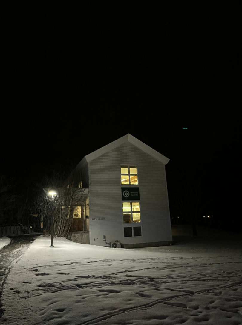 a picture of a dark night sky with snow on the ground. The white Hillel building is in the center.
