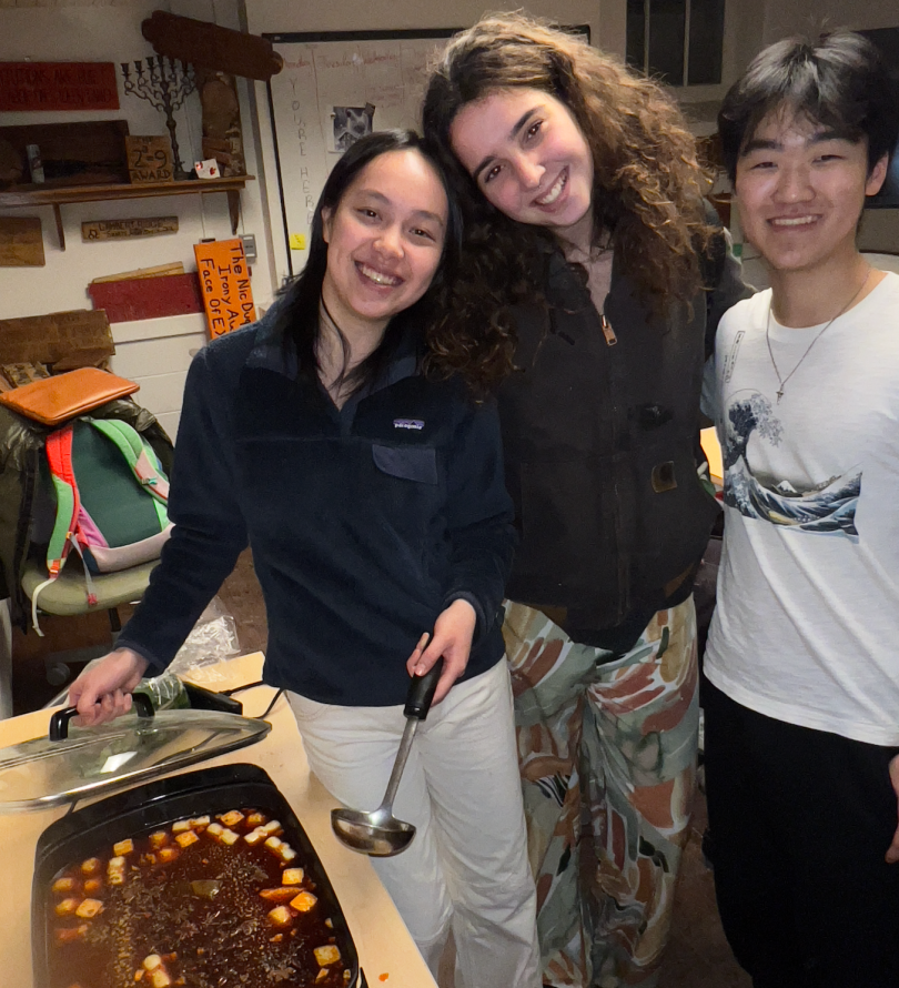 three people smiling with a freshly made hot pot in front of them