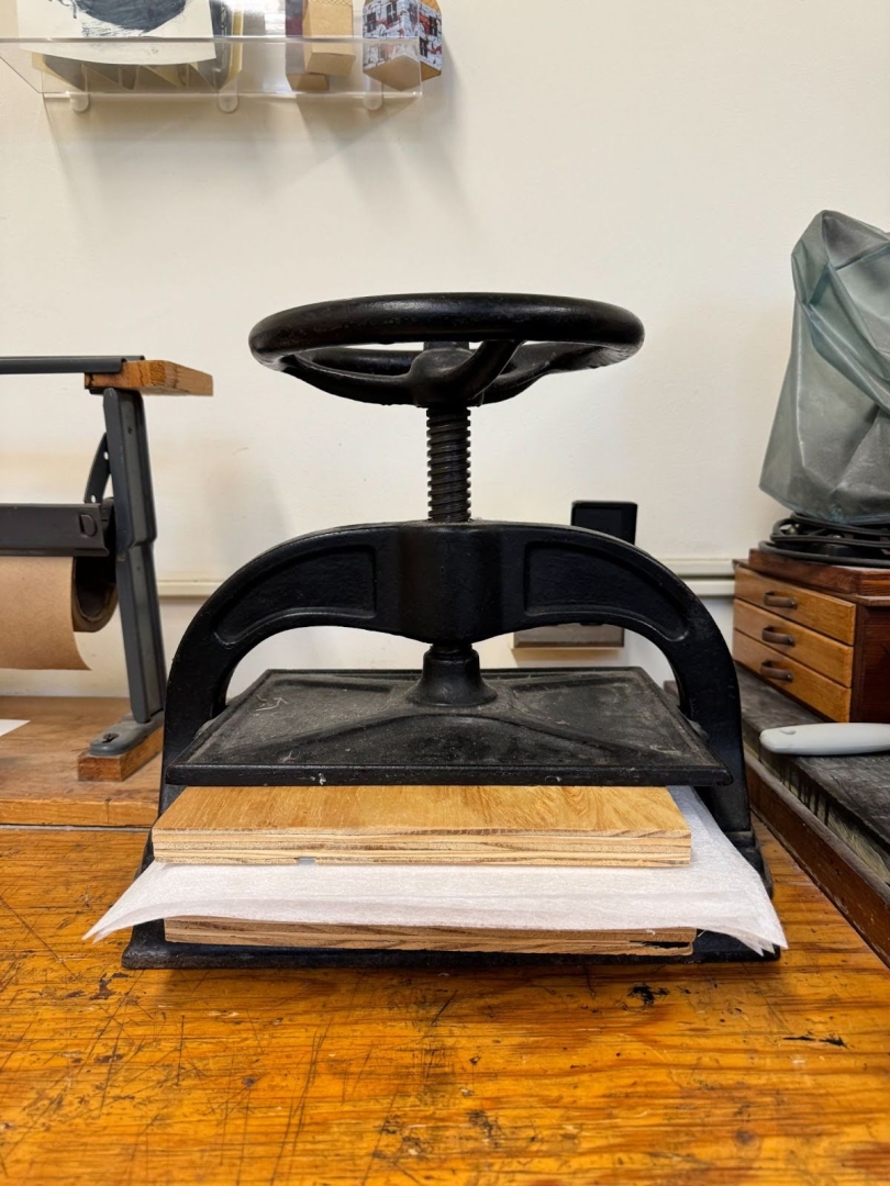 A black book press with plywood, papyrus, and blotting paper in it on a wooden desk.