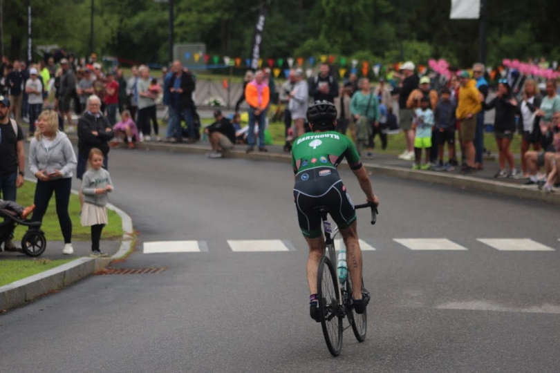 An image of a Dartmouth triathlete on a road bike from the rear surrounded by spectators.