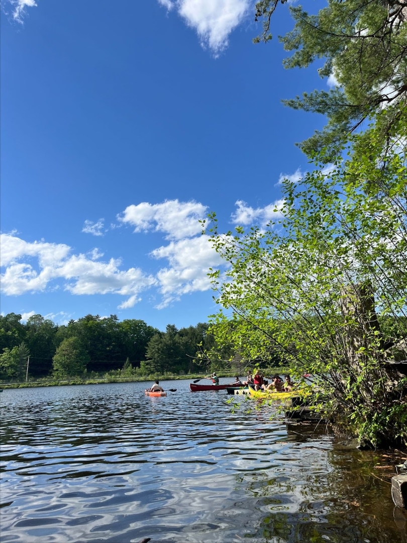 A few kayaks and canoes in the Connecticut on a sunny day. There are a few clouds in the bright blue sky.