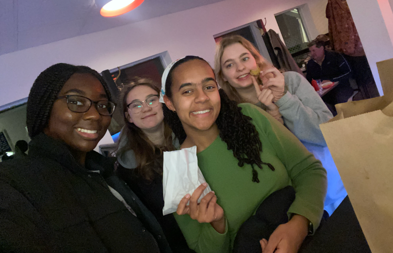 Four girls at a diner. One is holding a white bag of fries. 