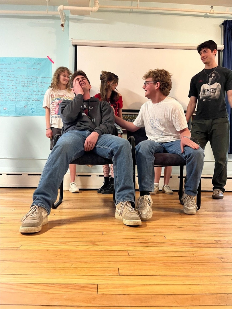 Two students are improving in chairs while 4 others stand waiting behind them.