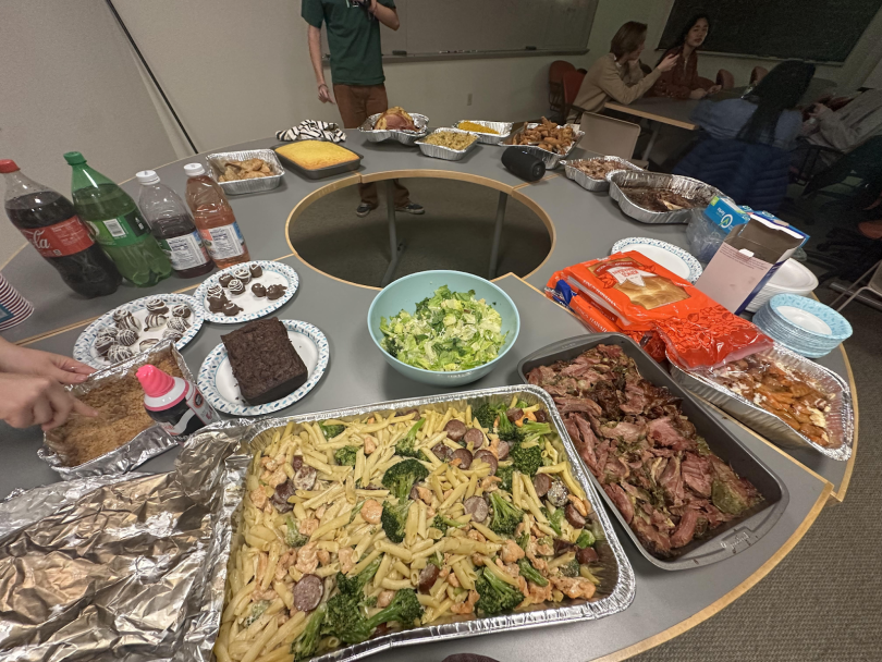 An array of dishes spread across a table: platters of pasta, soda, juice, assorted desserts, rolls, salads, and other festive foods. 