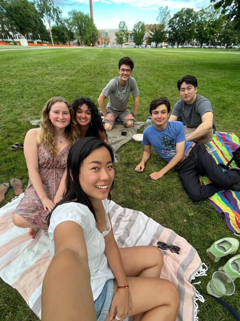 Six people smiling on the ground while sitting on picnic blankets.