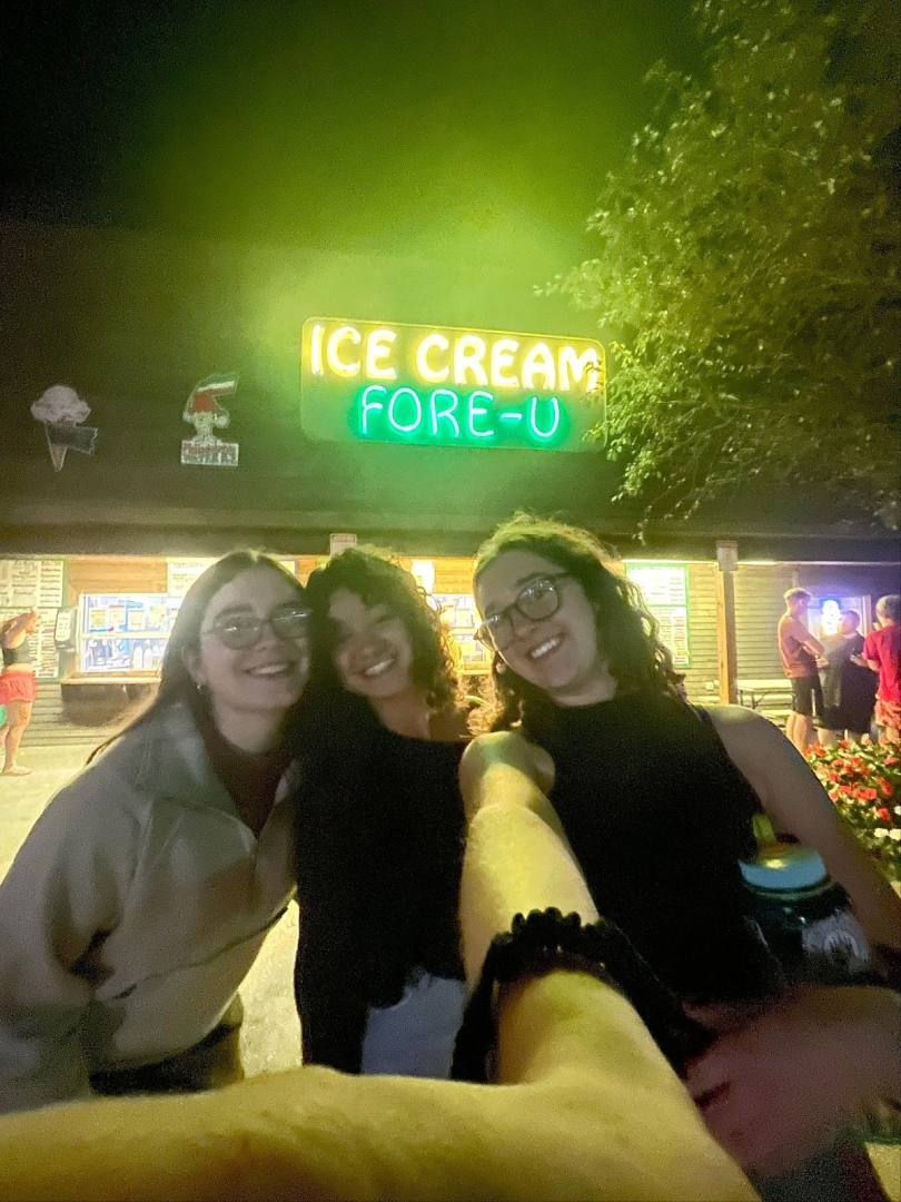 A selfie of three people standing in front of a glowing sign that reads "Ice Cream Fore-U"