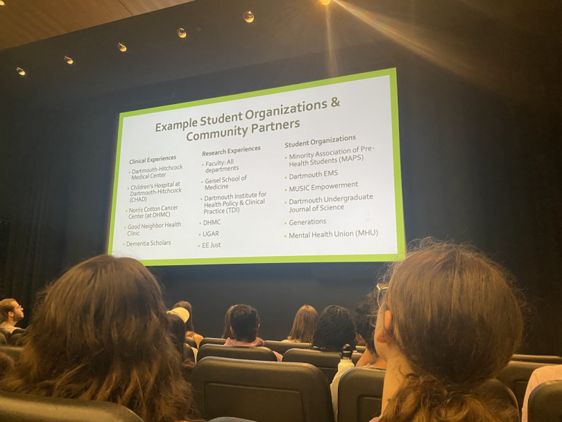 Students seated in an auditorium viewing a presentation slide listing Dartmouth student organizations, clinical experiences, and research opportunities.