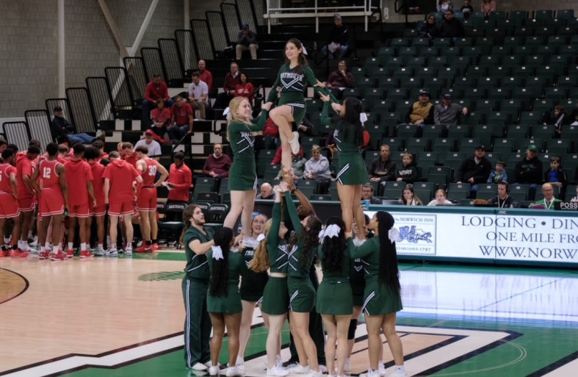 The Dartmouth cheerleaders performing a stunt in the middle of the basketball gymnasium, with a flyer in the center of the pyramid.