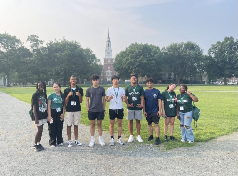 Picture of several Dartmouth Bound students posing for a picture in the middle of Dartmouth's green. In the background, several trees can be seen as well as Baker-Berry Library. 