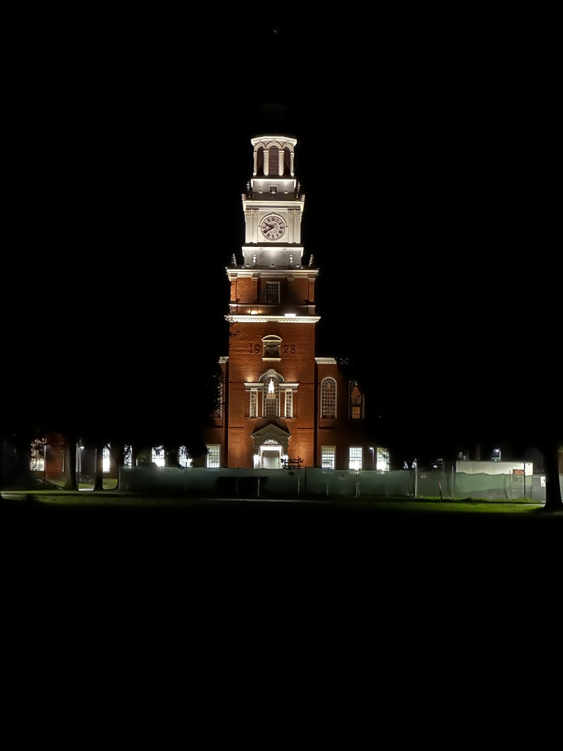 A picture of Baker-Berry Library at night. Several lights can be seen within the building as well as several exterior lights illuminating the Clock Tower.