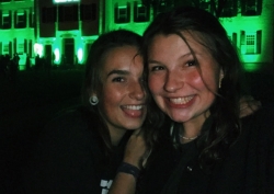 Abbi and a friend taking a selfie in front of Dartmouth Hall, which is lit in green for homecoming.