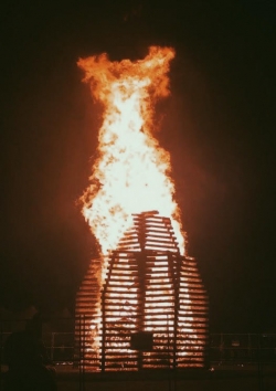 A large, burning bonfire behind 2 fences. 