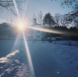 The sun rising in the background with a snowy path a white building in the foreground