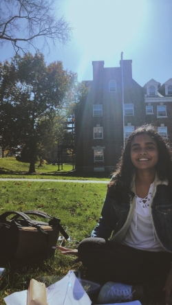 Abbi's friend sitting on the grass during an outdoor study session. A building and the sun are behind her.