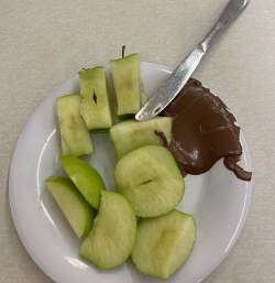 A picture of a Granny Smith apple on a plate with Nutella and a knife on the side.
