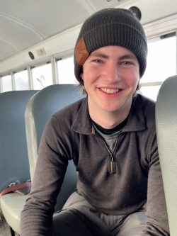 A photo of Aubrey smiling on a school bus. He is wearing a beanie.