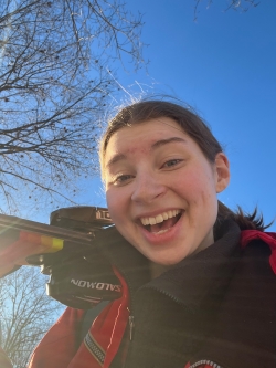 A selfie of me with a surprised and happy expression on my face. I am carrying my skis over my right shoulder. The sky is blue above me.