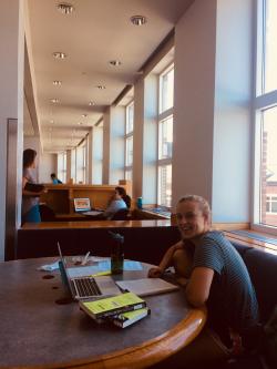 Margaret at table by window with books (other desks and students in background)