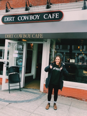 Abbi giving 2 thumbs up in front of Dirt Cowboy Cafe, a small coffee shop with lots of windows