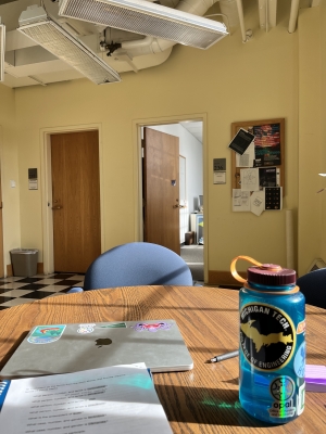 A photo of a table in Wilder Hall. On the table, there is a water bottle, laptop, and notebook. In the background, there are two doors and a bulletin board on the wall.
