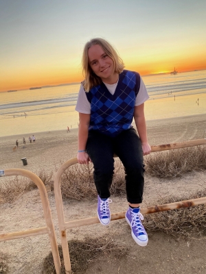 A picture of Cori smiling at the beach with the sunset behind her.