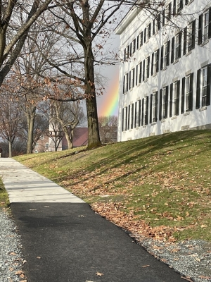 a picture of a sidewalk, the white facade of Reed Hall, and a rainbow in the background