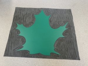 A maple leaf stamp carved into green and grey linoleum.
