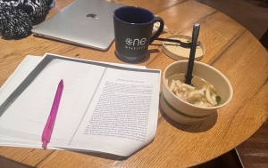 A copy of Virginia Woolf's short story "Phyllis and Rosamond" on a circular table next to a mug and a cup of chicken udon soup.