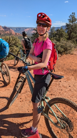 This is a photo of Lily sitting astride her bike on a short break with the landscape and a couple of other riders from the group behind her.
